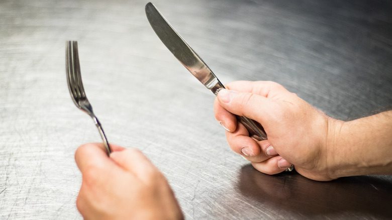 Knife and fork in hands on table