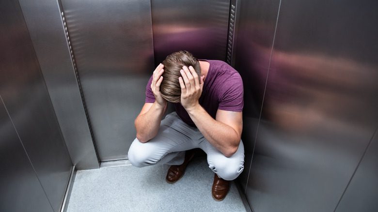 Homme accroupi piégé dans un ascenseur