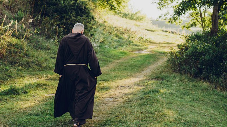 Moine catholique marchant sur un chemin forestier