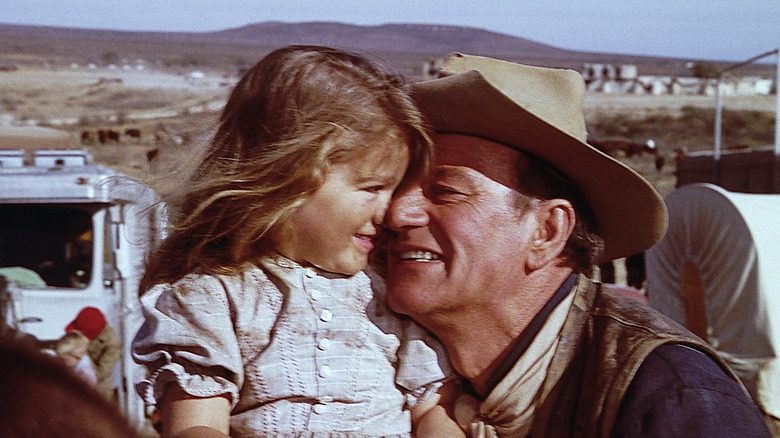 John Wayne souriant en cow-boy, embrassant une fille sur le plateau