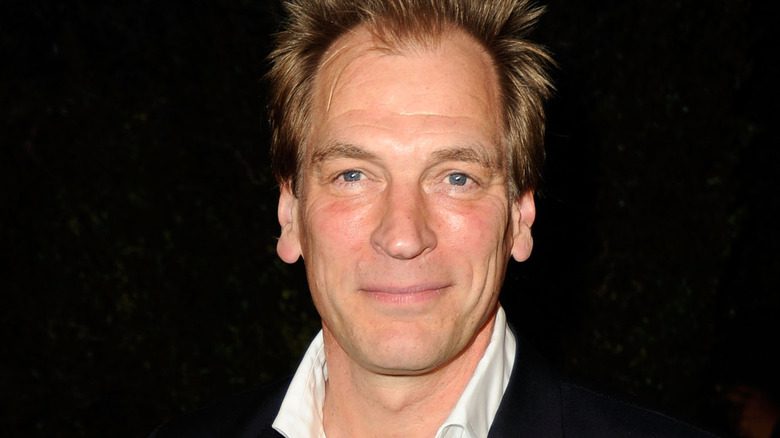 Julian Sands souriant sur fond noir