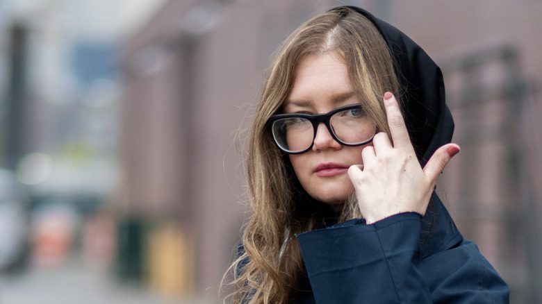 Anna Delvey avec un capuchon et des lunettes