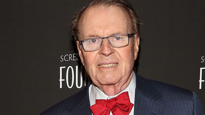 Charles Osgood souriant, portant des lunettes, un costume et un nœud papillon rouge