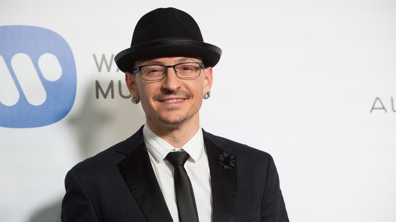 Chester Bennington souriant, portant un chapeau noir et un costume