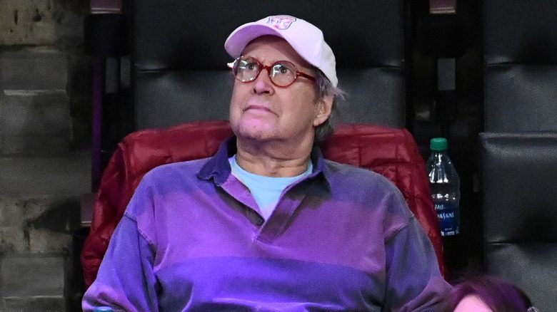 Chevy Chase en chemise violette et casquette blanche regardant vers le haut