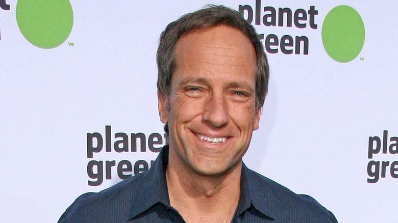 Mike Rowe souriant en chemise bleue, fond vert