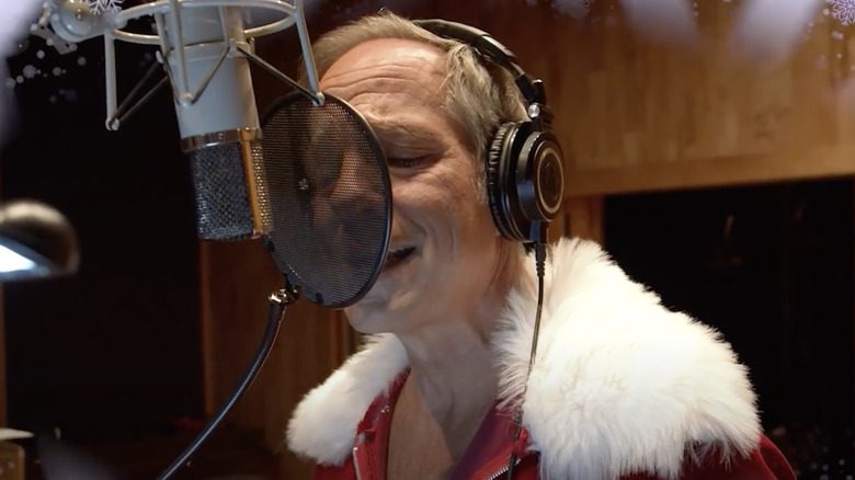 Mike Rowe en costume de Père Noël chantant dans un micro de studio