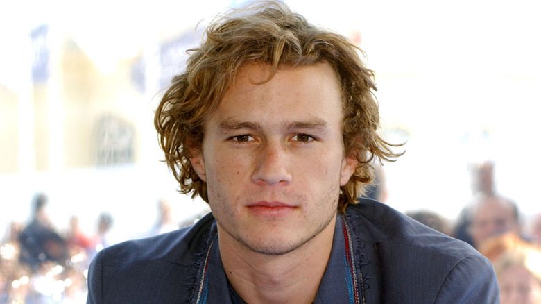 Heath Ledger avec des cheveux bouclés, en costume bleu, en extérieur