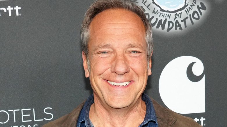 Mike Rowe souriant, en chemise en denim et veste en daim