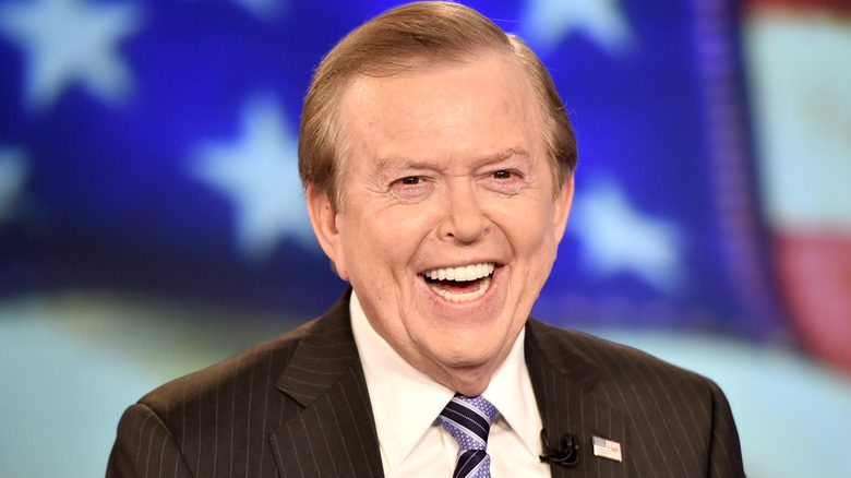 Lou Dobbs riant dans un costume avec le drapeau américain