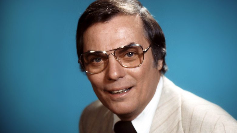 Peter Marshall souriant en costume crème et lunettes