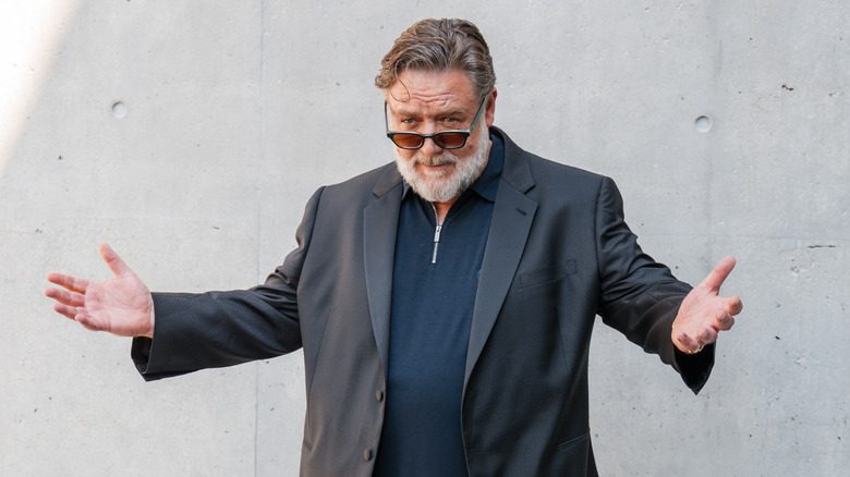 Russell Crowe dark jacket and sunglasses arms wide