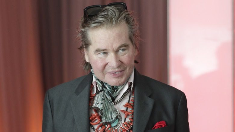 Val Kilmer souriant, costume, écharpe et collier