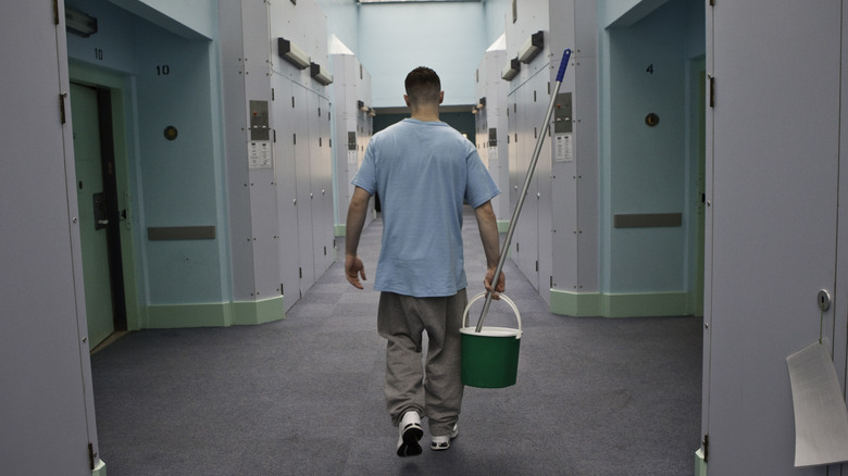 Prisonnier avec une serpillère et un seau marchant dans le couloir