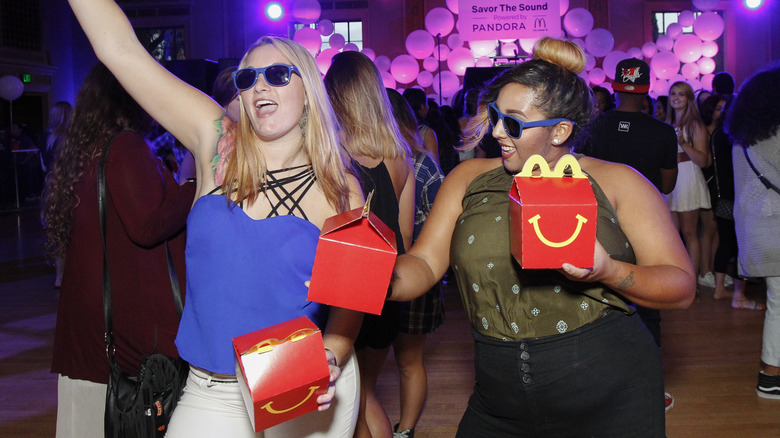 Des personnes portant des lunettes de soleil criant lors d'un concert avec des Happy Meals