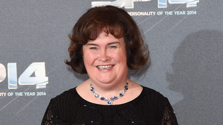 Susan Boyle souriante en robe noire et collier argenté