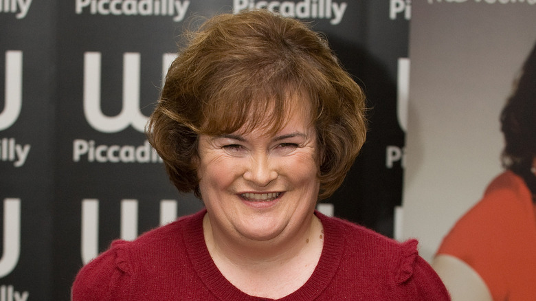 Susan Boyle souriante en pull rouge