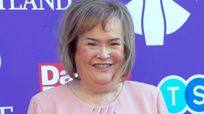 Susan Boyle souriante en robe rose avec des joues roses