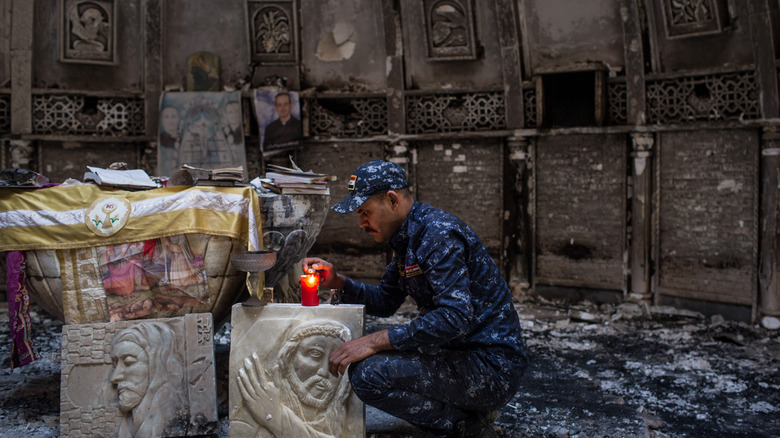 Soldat chrétien syrien allumant une bougie dans une église brûlée