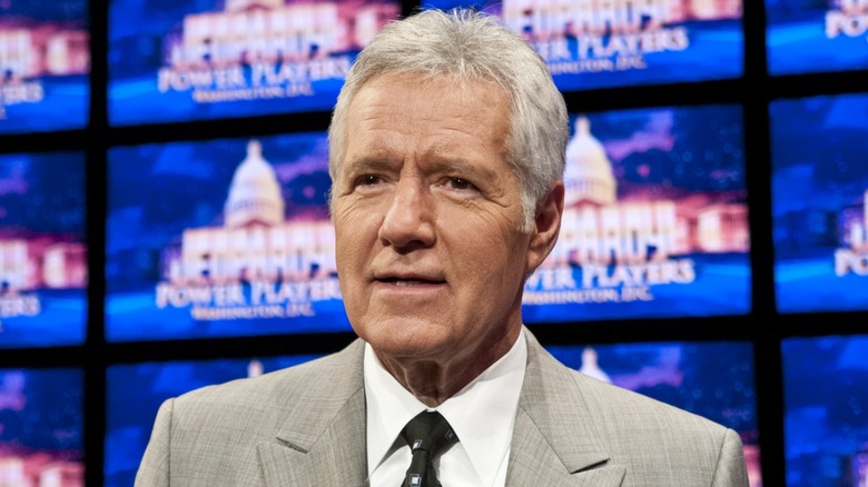 Alex Trebek souriant devant le plateau de Jeopardy