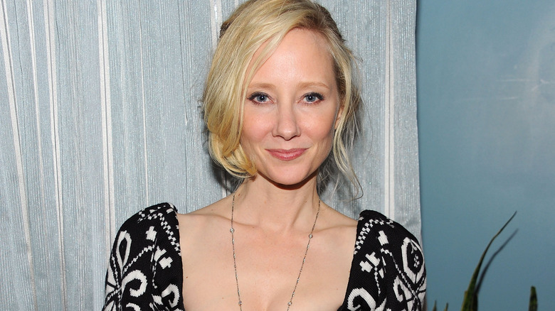 Anne Heche souriante vêtue d'une robe près d'un rideau