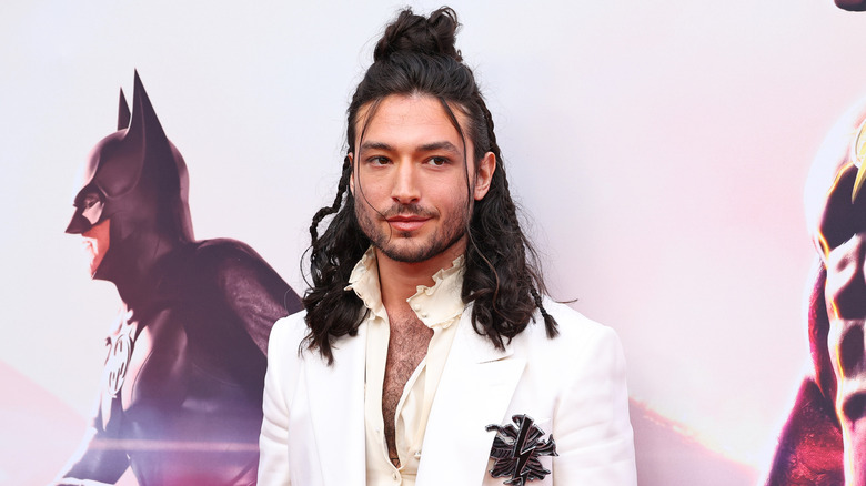 Ezra Miller avec de longs cheveux, portant du blanc et posant sur le tapis rouge