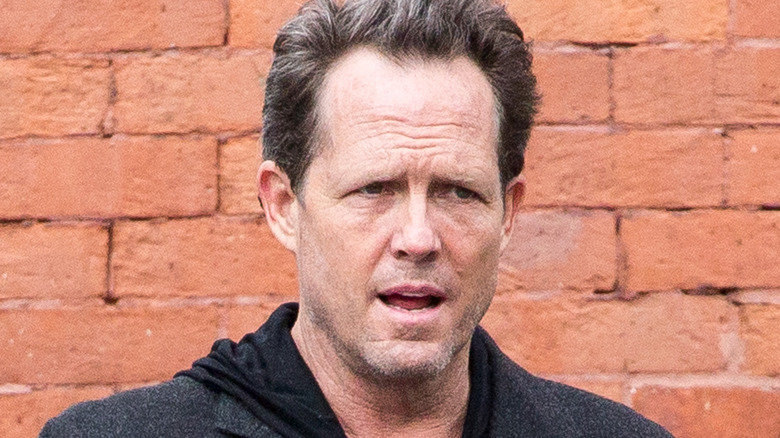 Dean Winters marchant devant un mur en briques