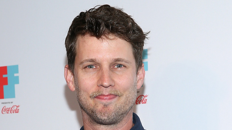 Jon Heder grimace devant une publicité Walmart lors d'un événement