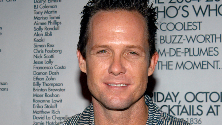 Dean Winters portant une chemise rayée, souriant et plissant les yeux