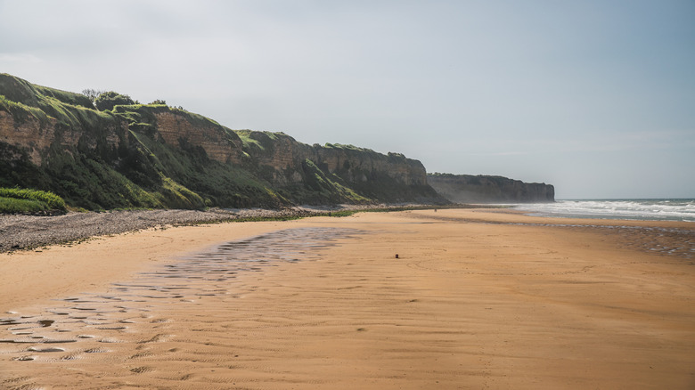 Vue moderne de la plage d'Omaha en Normandie, France, avec l'océan à droite et les falaises à gauche.