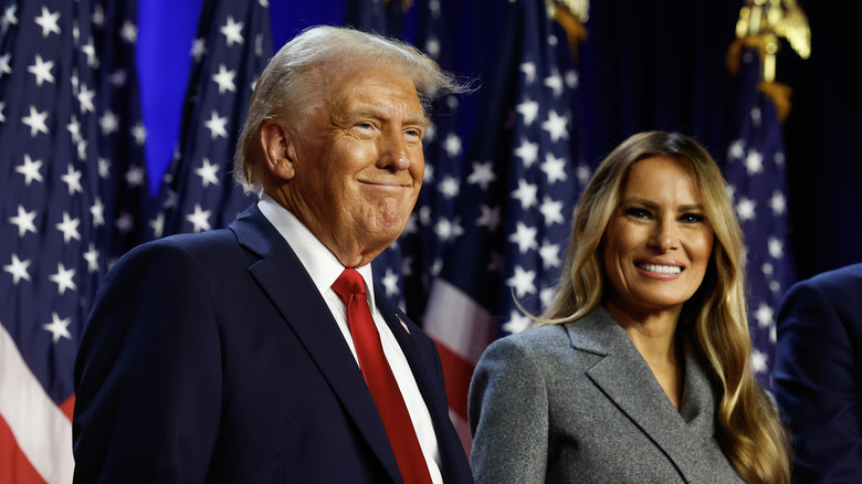 Donald et Melania Trump souriant sur scène devant des drapeaux