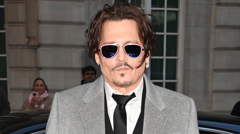 Johnny Depp portant des lunettes de soleil, un manteau gris et une cravate noire