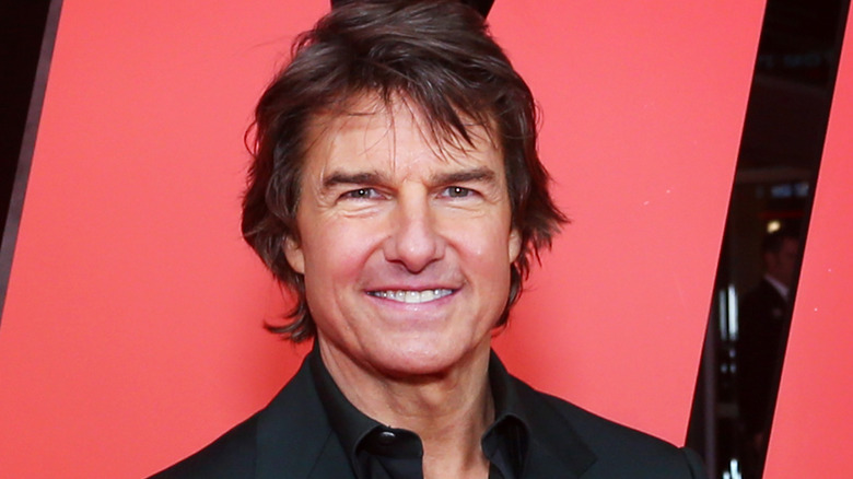 Tom Cruise souriant devant une grande affiche de Mission: Impossible