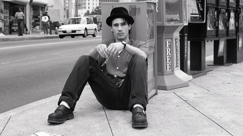 Jeff Buckley portant un chapeau noir assis à un coin de rue