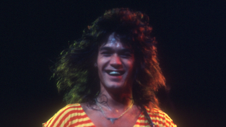 Eddie Van Halen souriant en jouant dans une combinaison jaune et rouge