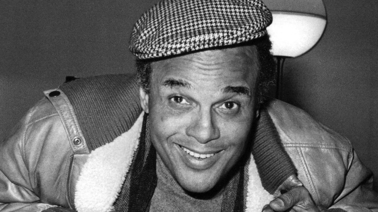 Harry Belafonte souriant de manière ludique avec un chapeau et une veste en cuir