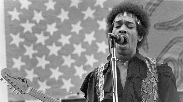 Jimi Hendrix chantant et jouant de la guitare devant un fond de drapeau américain