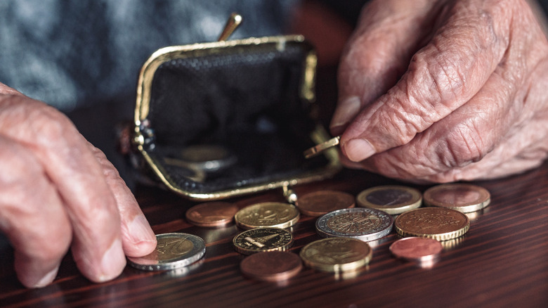 Les mains d'une personne âgée avec des pièces et un porte-monnaie