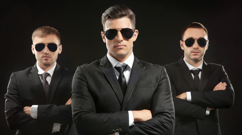 Trois hommes en costume noir avec des lunettes de soleil sur fond sombre