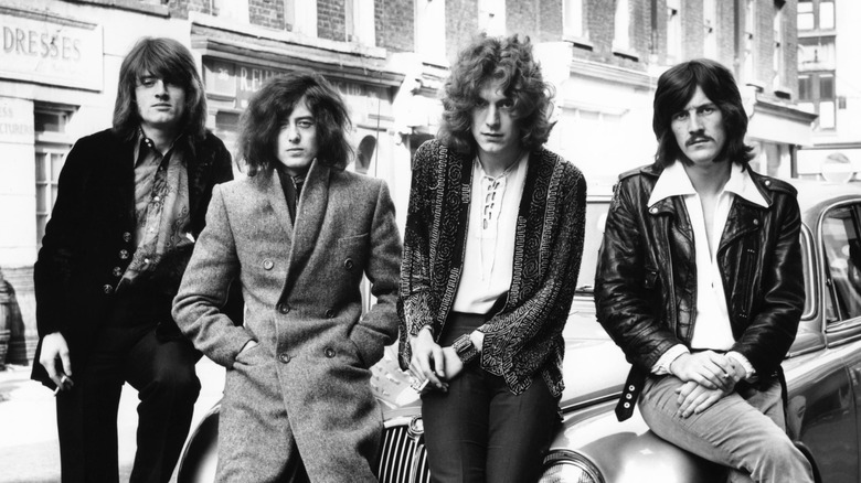 Membres de Led Zeppelin posant sur le capot d'une voiture dans une rue urbaine