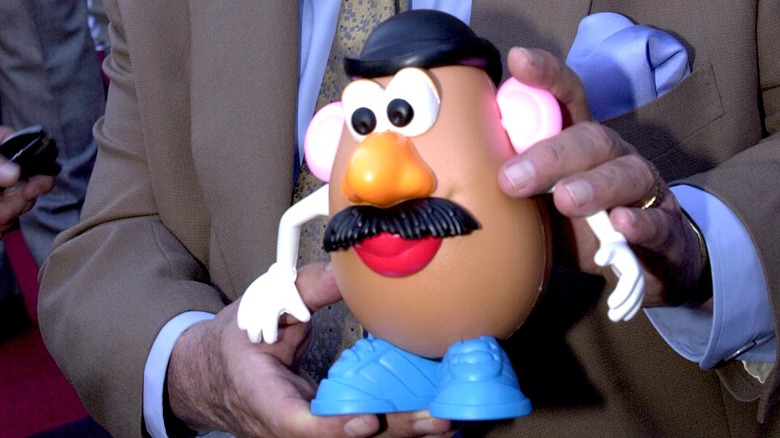 Un homme en costume tient Mr. Potato Head