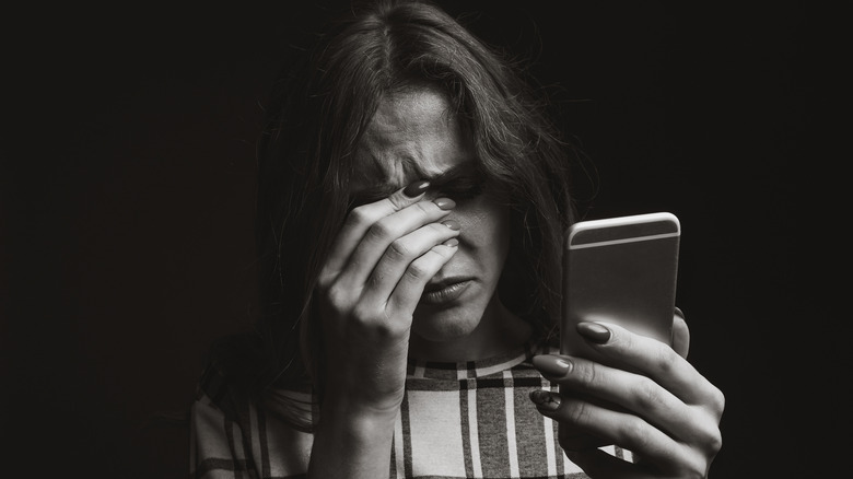 Woman with phone gripping brow