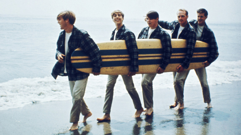 Les Beach Boys sur une plage avec une planche de surf